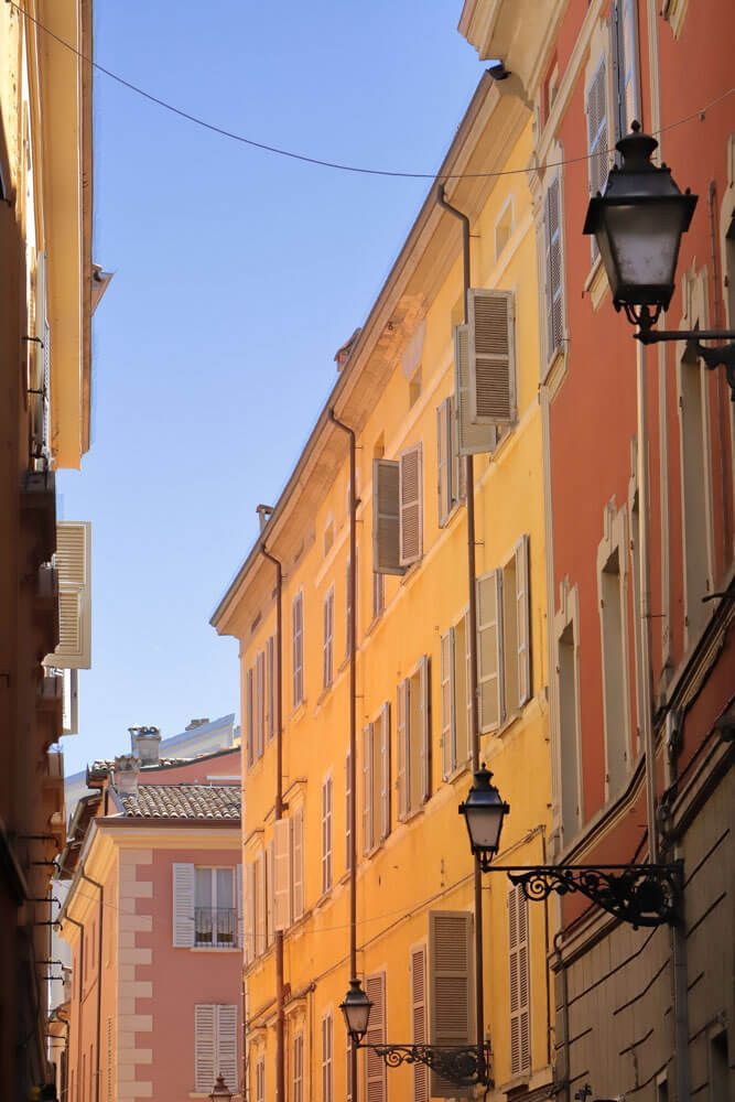 Strada del centro storico di Parma con palazzi dalle facciate arancio e ocra e lampioni in ferro battuto.
