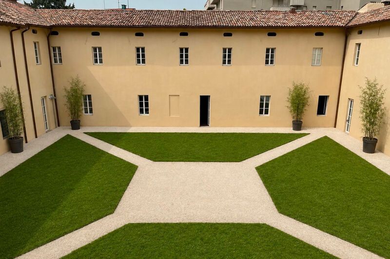 Il Chiostro 26 interno con prato verde attraversato da vialetti in ghiaia chiara, circondato dalla facciata settecentesca color ocra.
