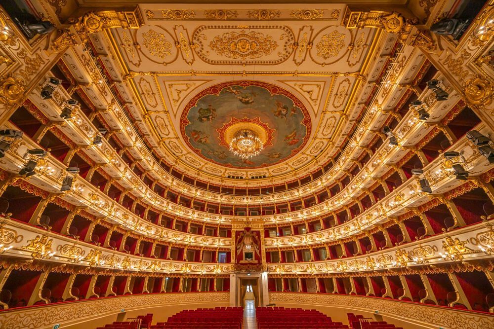 Interno del Teatro Regio di Parma con i palchi decorati in oro e rosso disposti a ferro di cavallo e il soffitto affrescato con lampadario.