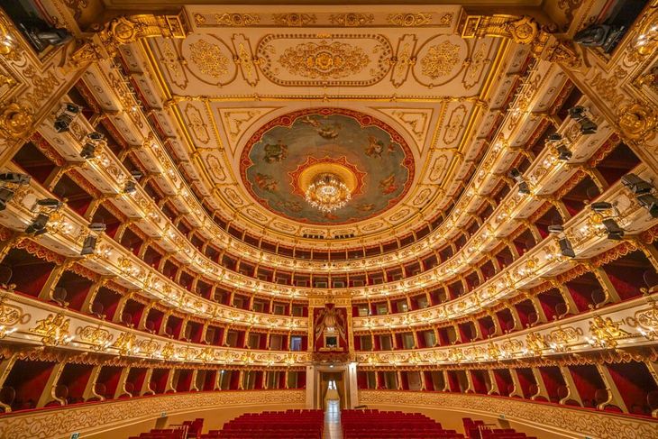 Interno del Teatro Regio di Parma con i palchi decorati in oro e rosso disposti a ferro di cavallo e il soffitto affrescato con lampadario.