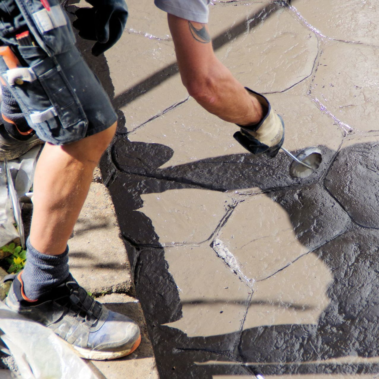 Homme créant un motif en béton avec un outil sur une terrasse.