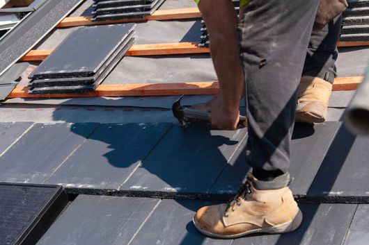 Ouvrier installant des tuiles sombres sur un toit en construction.