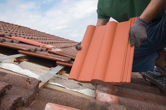 Ouvrier installant des tuiles sur un toit endommagé.