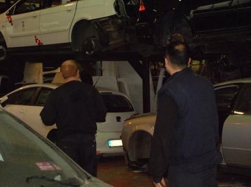Dos hombres están parados frente a una pila de autos en un garaje.