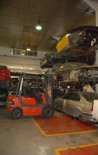 Un hombre conduce una carretilla elevadora en un garaje con coches apilados uno encima del otro.