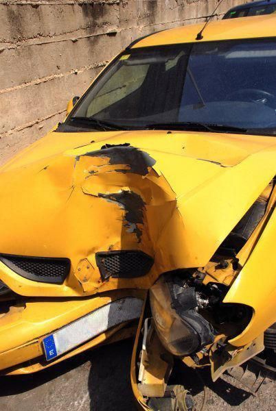 Un coche amarillo con el frontal dañado está aparcado delante de un muro.