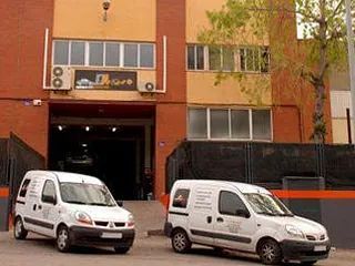 Dos furgonetas blancas están estacionadas frente a un edificio.