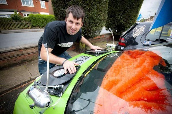 Un hombre está de pie junto a un coche verde con un tocadiscos en el capó.