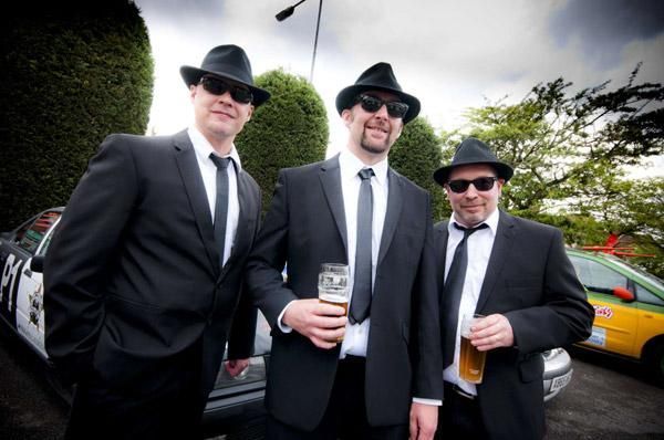 Tres hombres con trajes y sombreros están parados uno al lado del otro.