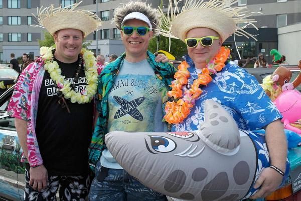 Tres hombres posan para una foto y uno de ellos sostiene un tiburón inflable.