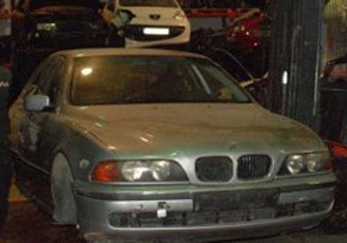 Un BMW está sentado encima de una pila de otros coches en un garaje.
