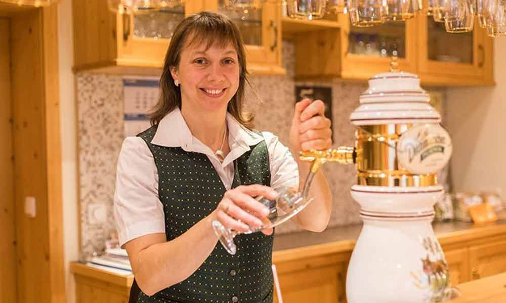 Eine Frau gießt in der Küche eine goldene Flüssigkeit in ein Glas neben einer weißen Apfelweinpresse.