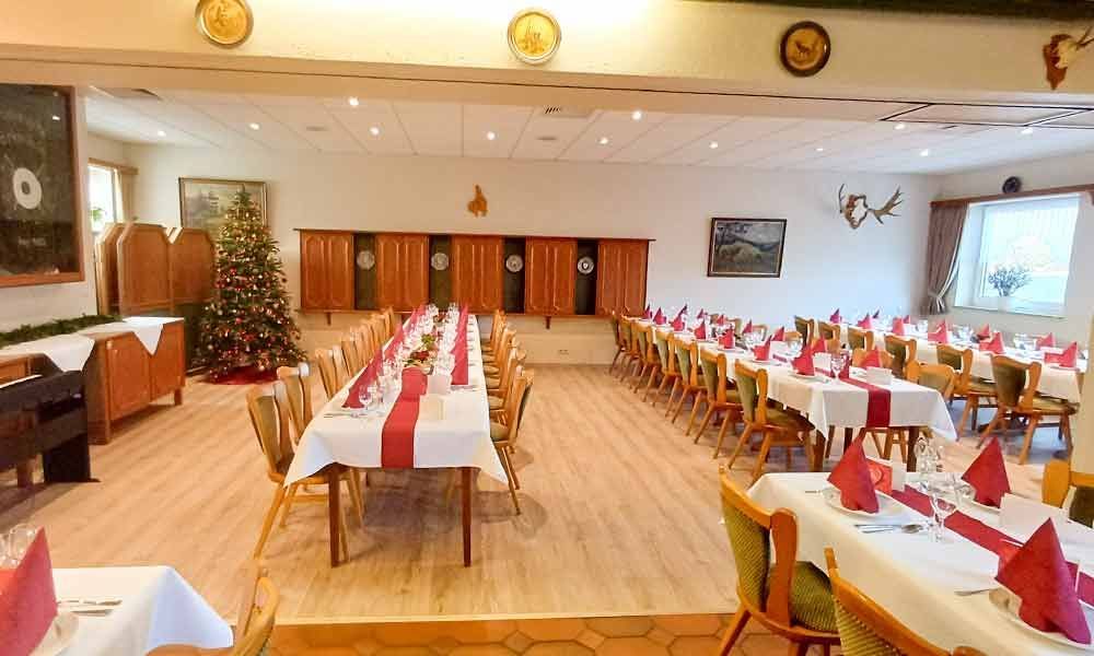 Ein leerer Festsaal, gedeckt für ein Essen, mit langen Tischen, weißen Stühlen, roten Servietten und einem geschmückten Baum.