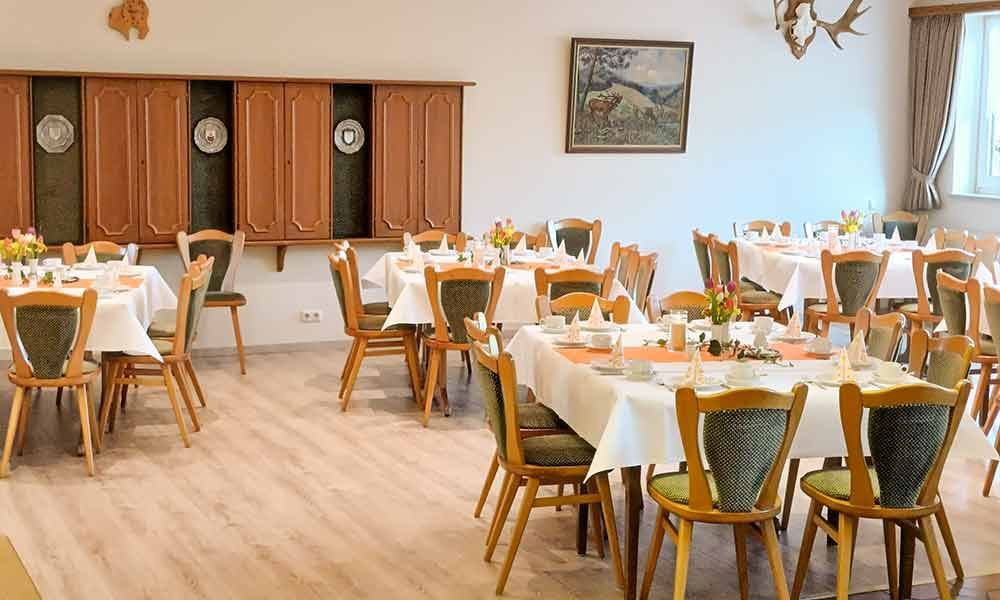 Helles Esszimmer mit runden Tischen, weißen Tischdecken, Holzstühlen und Wanddekoration