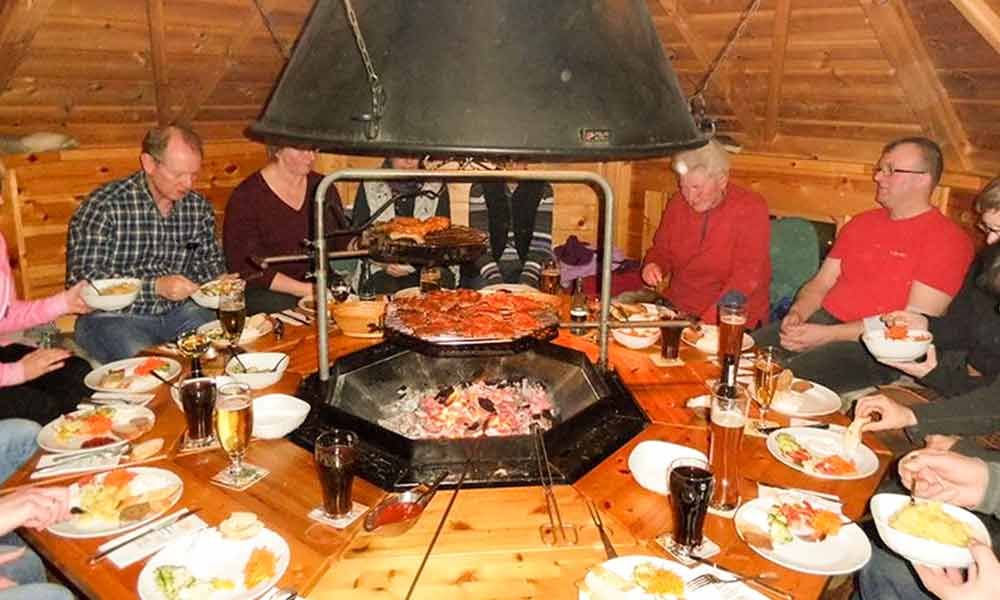 Gemeinsames Essen an einem brutzelnden Tischgrill in einem gemütlichen Restaurant mit Tellern, Getränken und Gerichten zum Teilen.