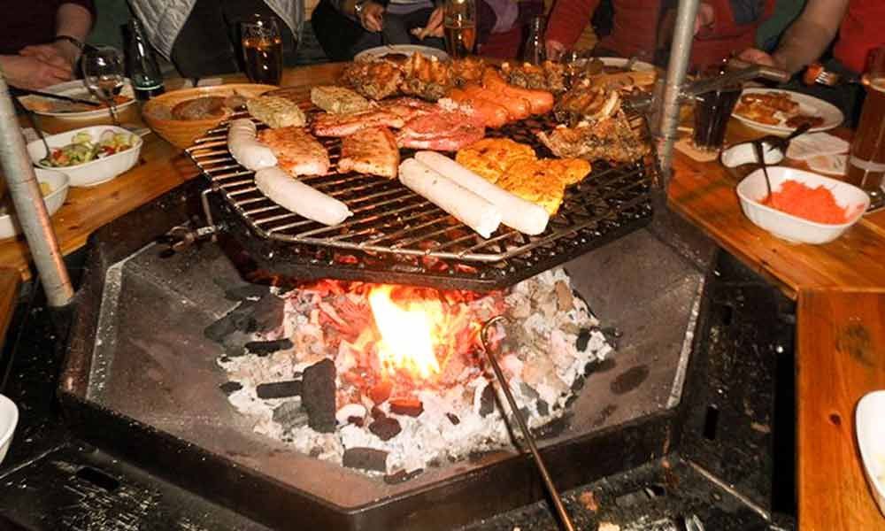 Fleisch und Gemüse werden auf einem offenen Holzkohlefeuer an einem Restauranttisch gegrillt