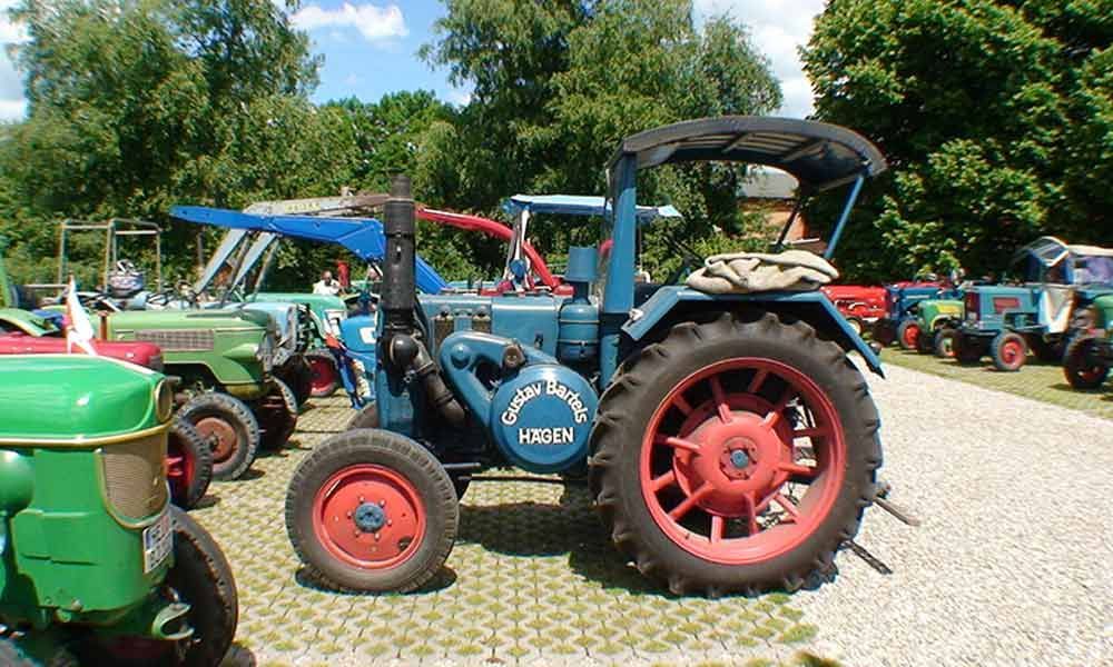 Blauer Oldtimer-Traktor mit roten Rädern und Verdeck, der im Freien zwischen anderen alten Traktoren parkt.
