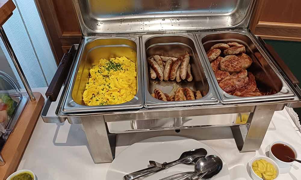Frühstücksbuffet mit Rührei, Würstchen und gebratenen Hähnchenteilen auf einem Frühstückstisch
