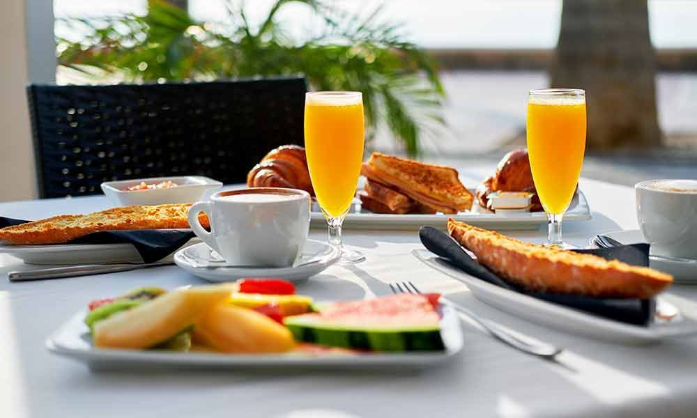 Frühstückstisch mit Orangensaft, Kaffee und Tellern mit Essen an einem hellen Fenster