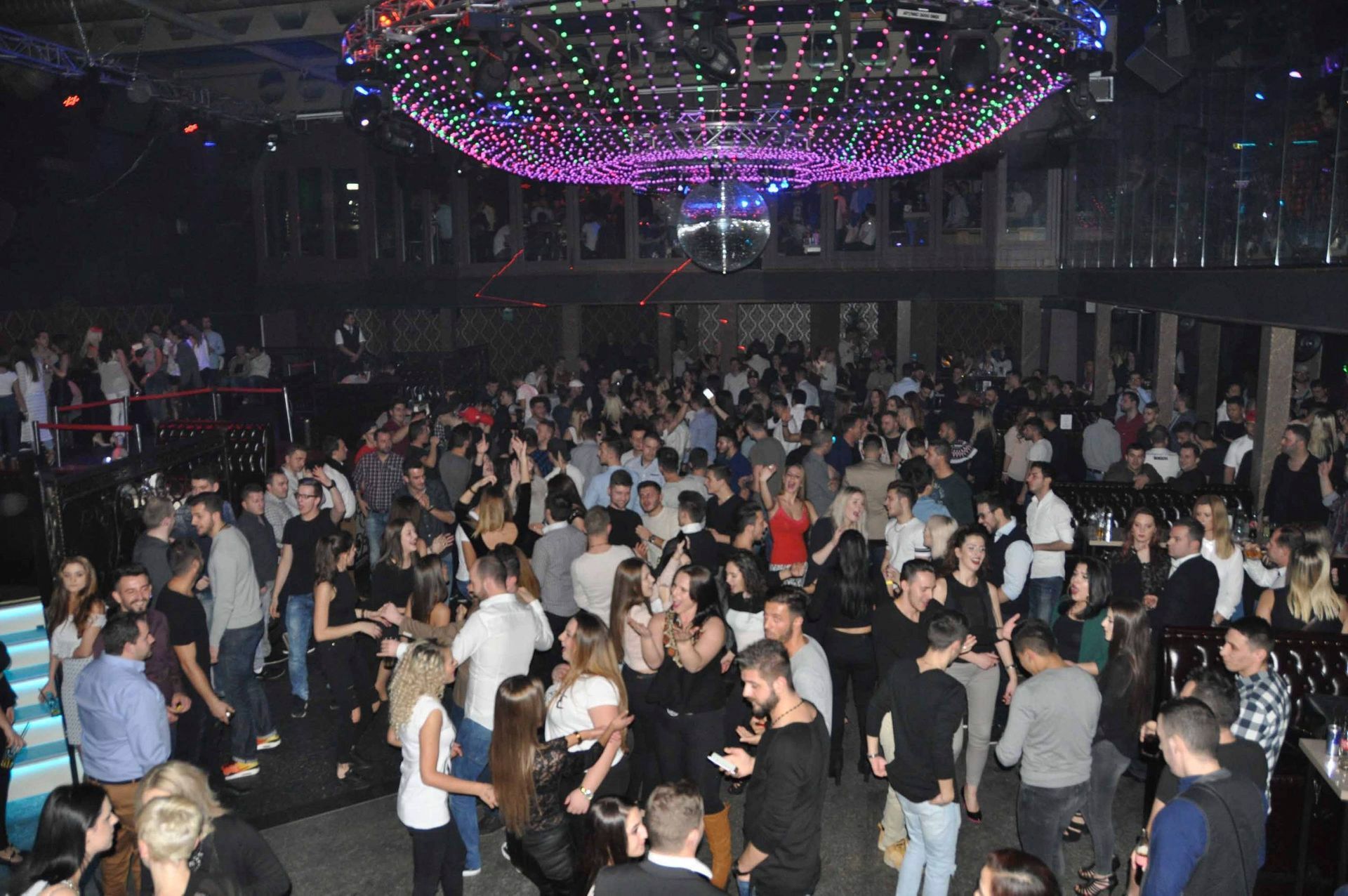 Volle Tanzfläche in einem Nachtclub, auf der sich die Menschen unter bunten Deckenlichtern mischen.