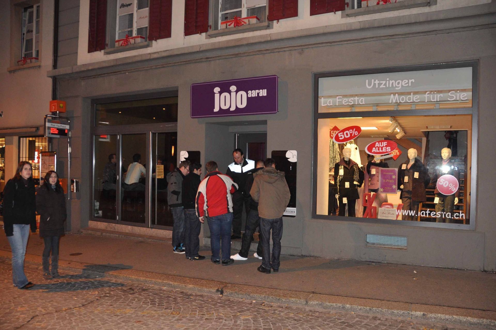 Nachts versammelten sich Menschen vor einem lilafarbenen Ladenlokal; die Schaufenster waren beleuchtet