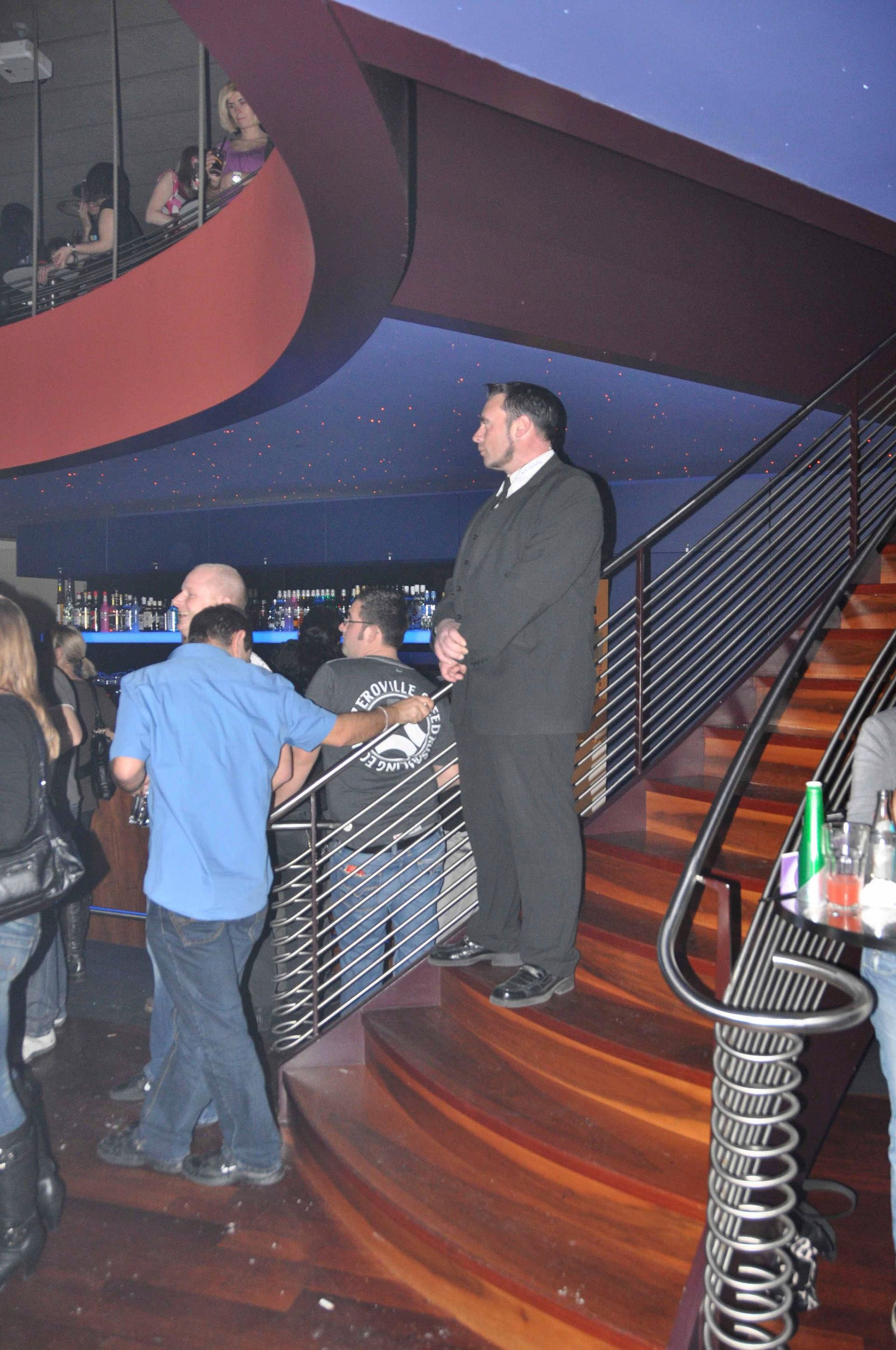 Menschen stehen auf einer geschwungenen Treppe in einem schwach beleuchteten Club oder einer Bar