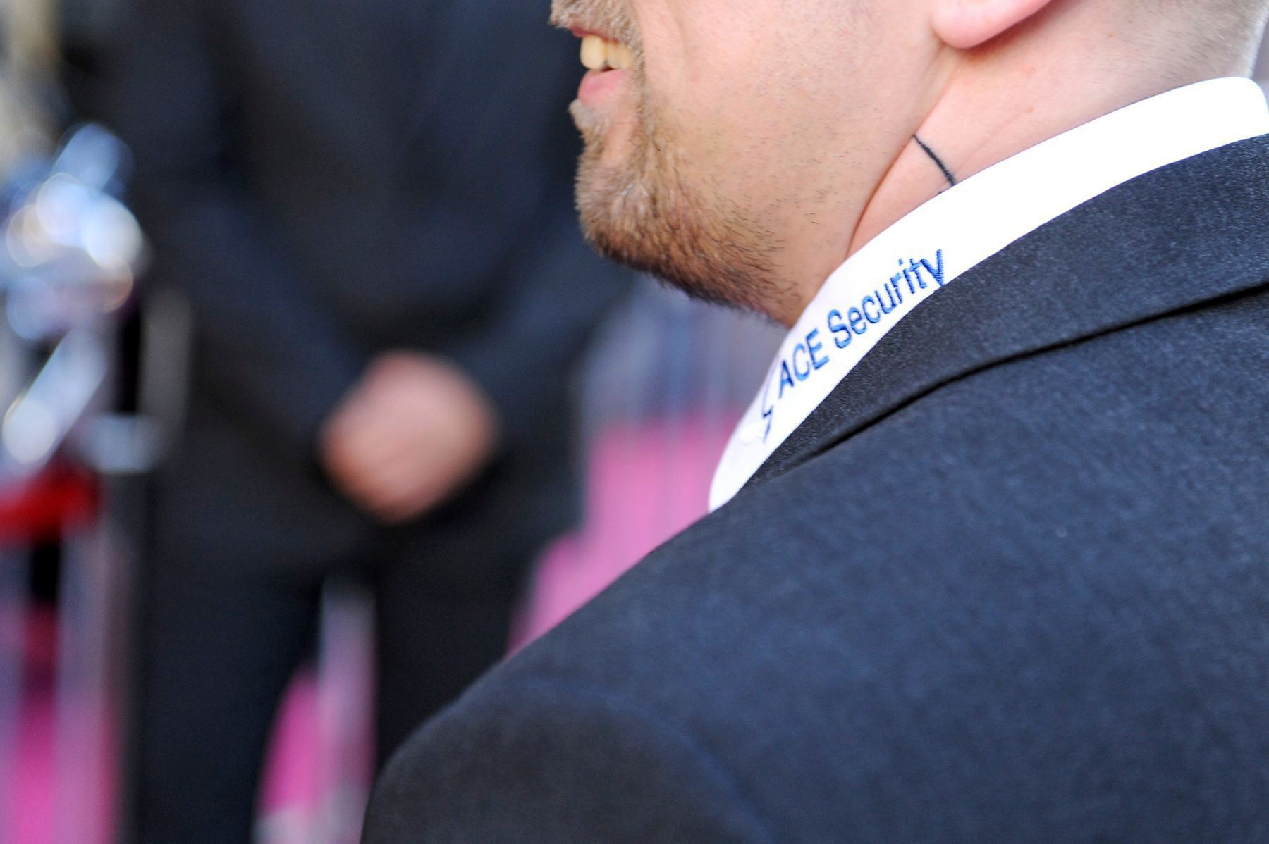 Mann in einem dunklen Blazer mit weißem Kragen und der Aufschrift „Security“ bei einer formellen Veranstaltung