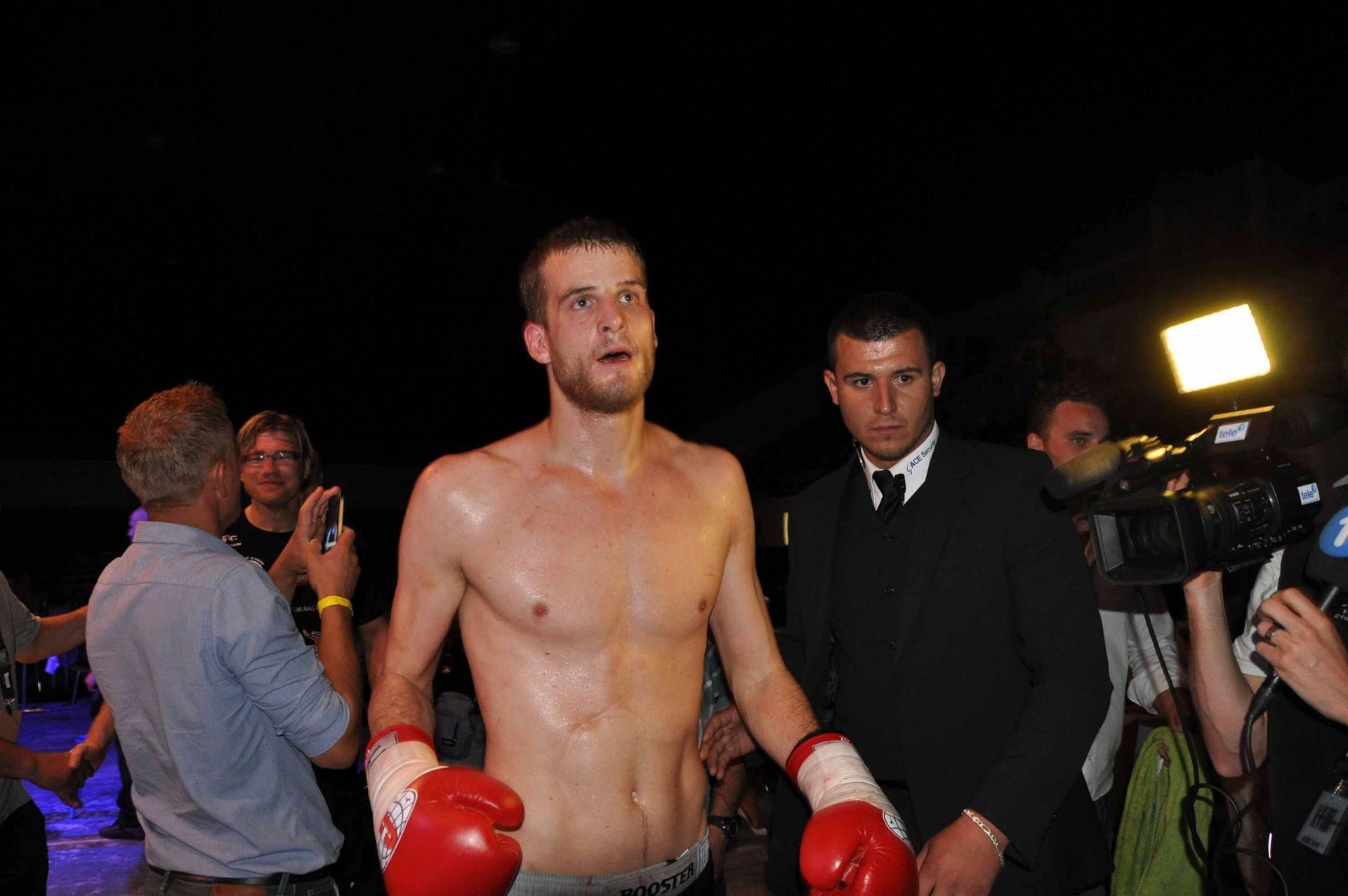 Ein Boxer mit roten Boxhandschuhen steht im Ring, der von Kamerascheinwerfern beleuchtet wird