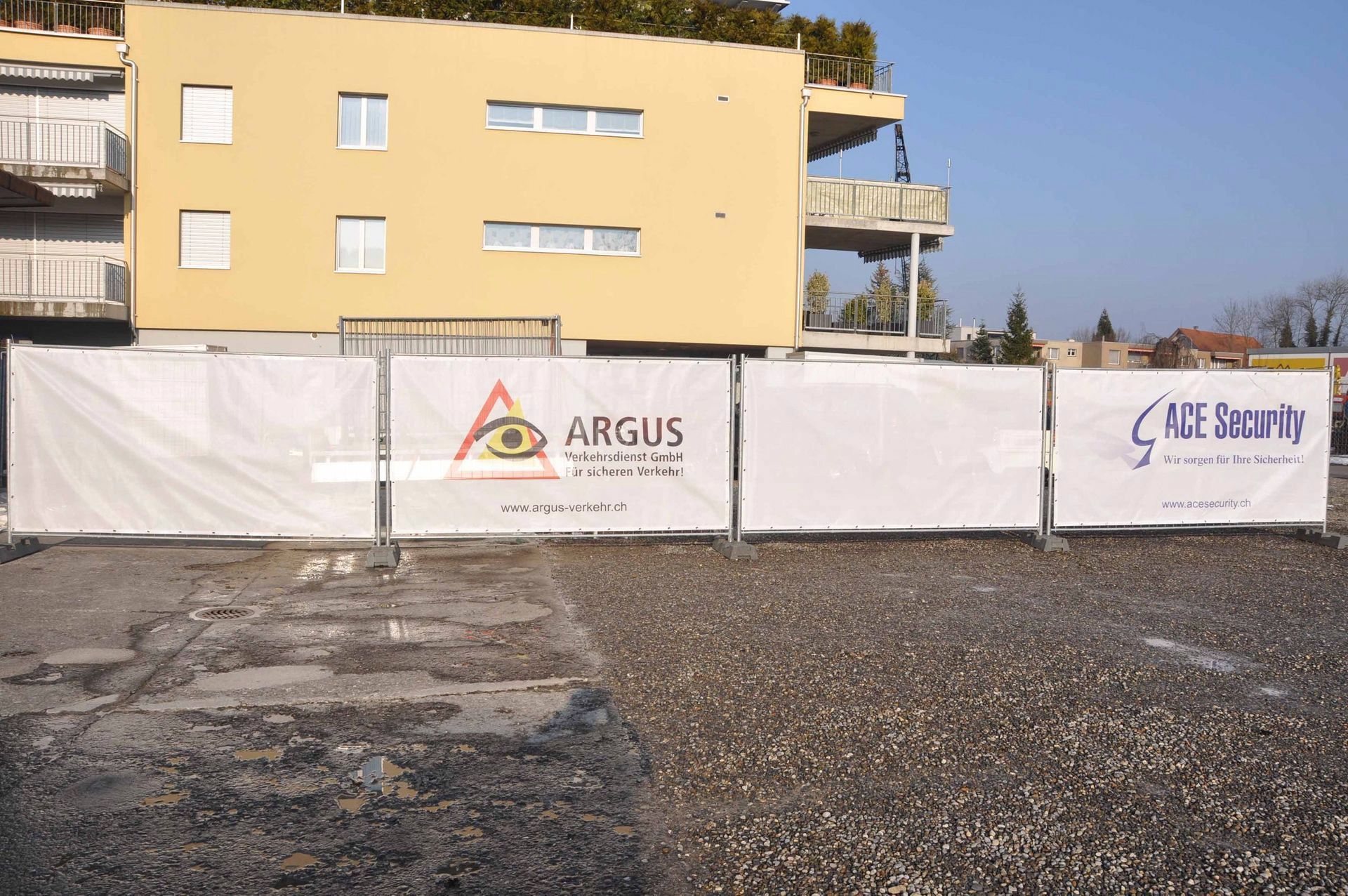 Baustelle mit weißen Zaunbannern vor einem gelben Gebäude