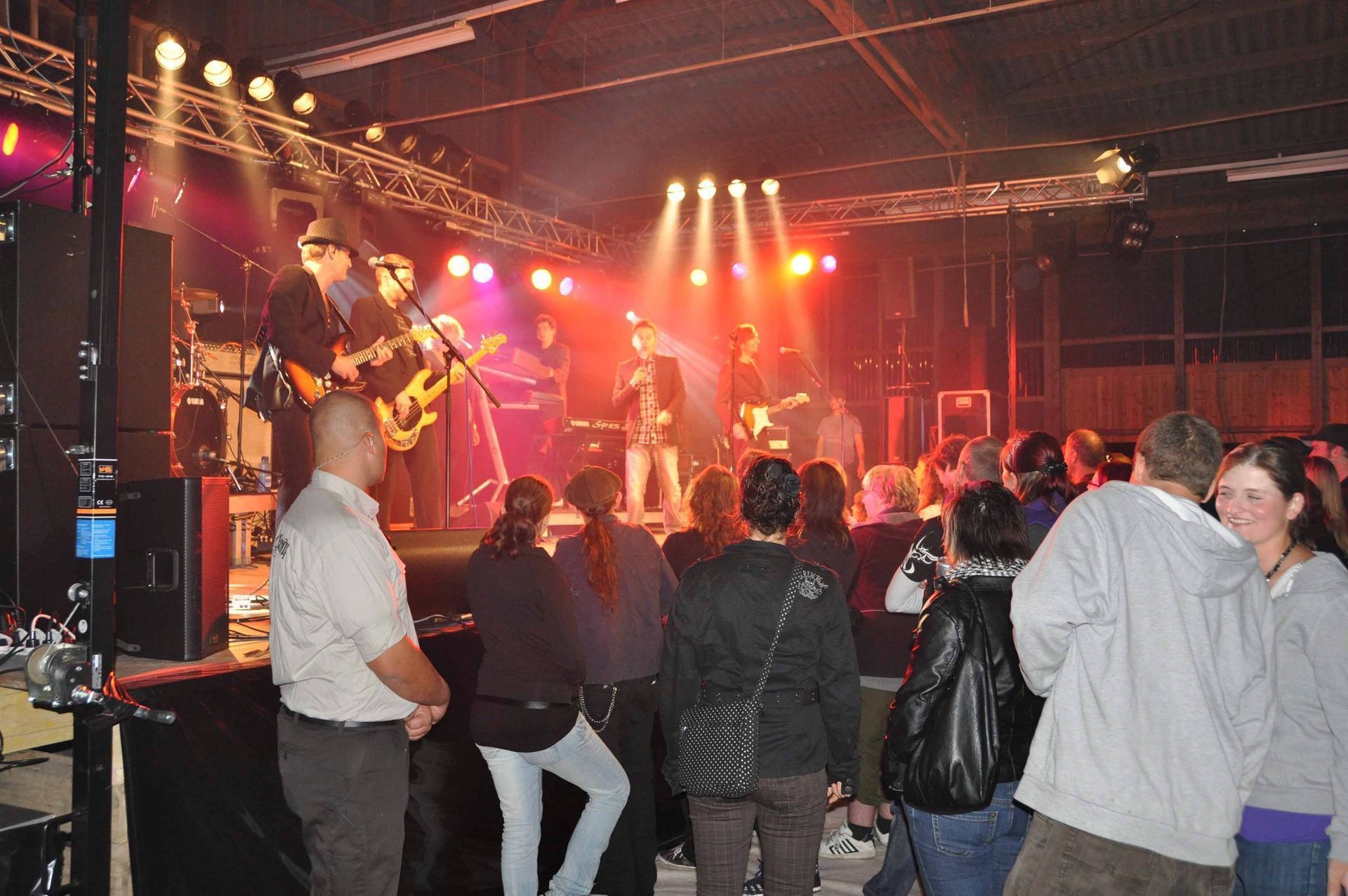 Eine Live-Band spielt auf einer rot beleuchteten Bühne, während das Publikum steht und zuschaut.