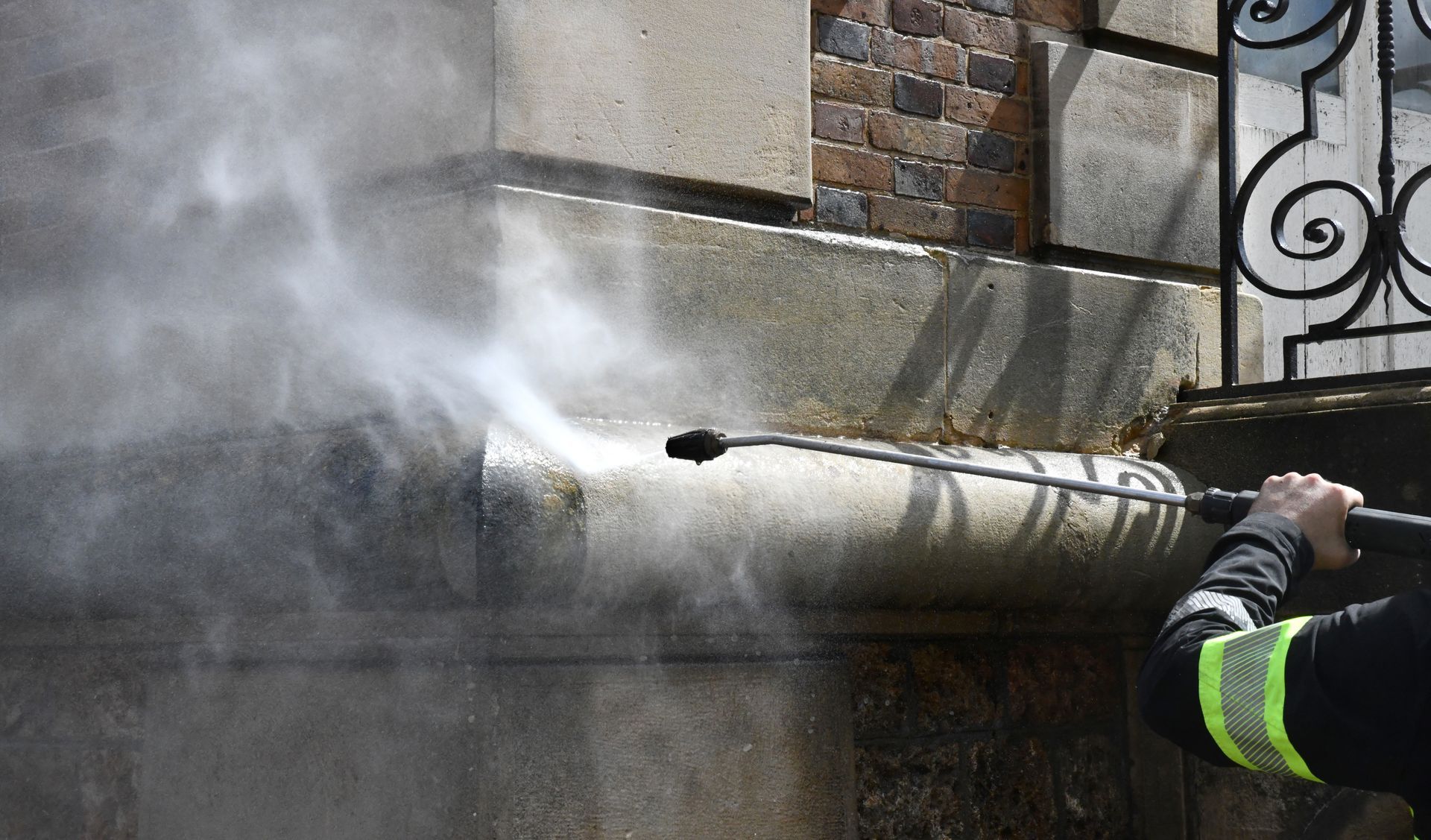 Une personne nettoie à haute pression la façade d'un bâtiment en pierre, créant un nuage de brume.