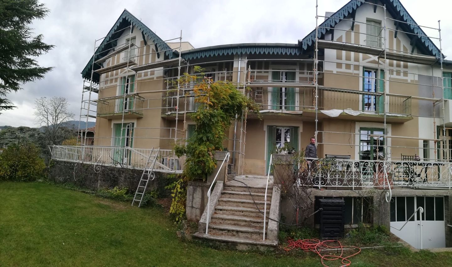 Un homme se trouve devant une maison sur laquelle un échaffaudage est placé sur toute la facade qui semble nouvellement refaite