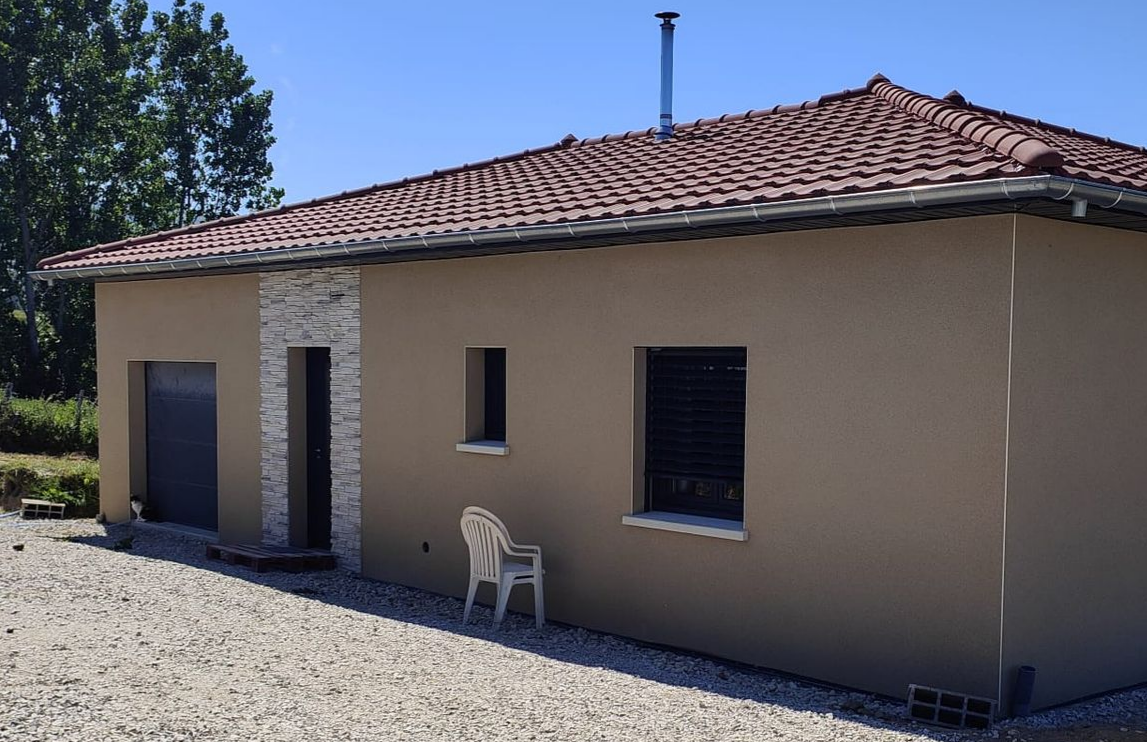 Une maison avec une façade refaite à neuf, deux chaises en plastique sont empilées contre le mur, on voit la porte d'entrée et l'entrée du garage.