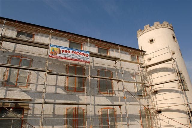 La facade d'un chateau avec un échaffaudage sur lequel il y a une pancarte de la société pro façades