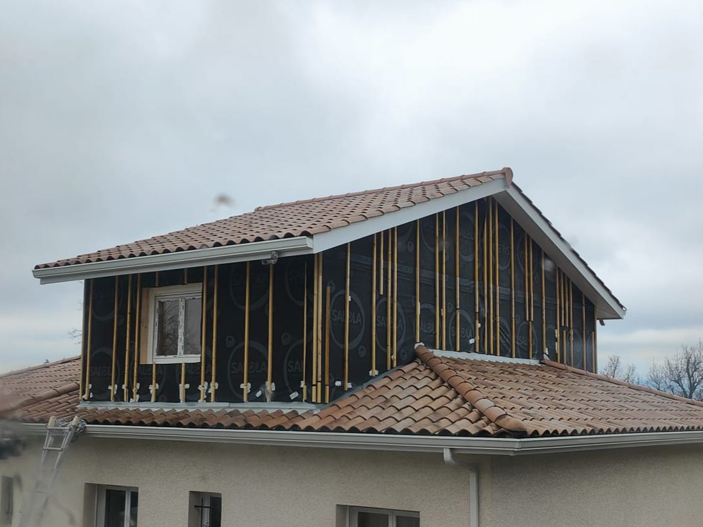 Bâtiment en construction avec bardage beige, balcons et charpente en bois apparente.