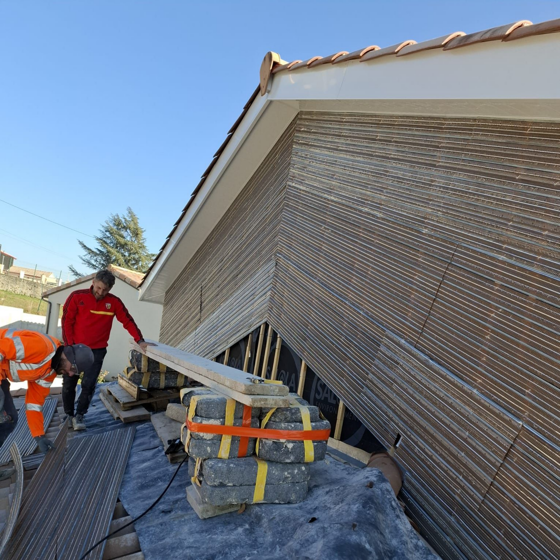Bâtiment en cours de rénovation ; échafaudages, isolation jaune sur le côté, bardage gris.