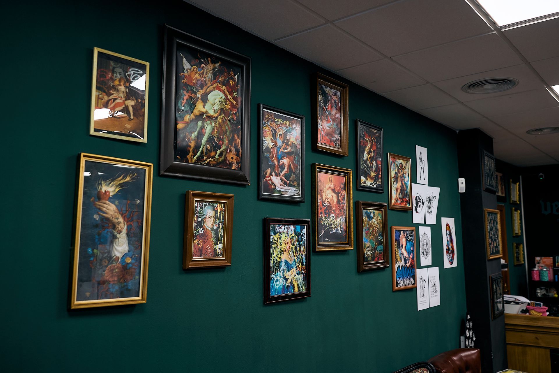 Galería de obras de arte enmarcadas en una pared verde oscuro de un pasillo, con una variedad de pinturas y bocetos coloridos.