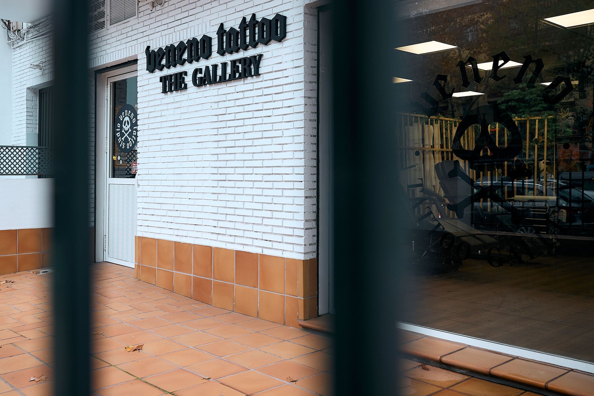 Exterior de una galería con pared de ladrillo blanco, azulejos naranjas y puerta metálica en primer plano.