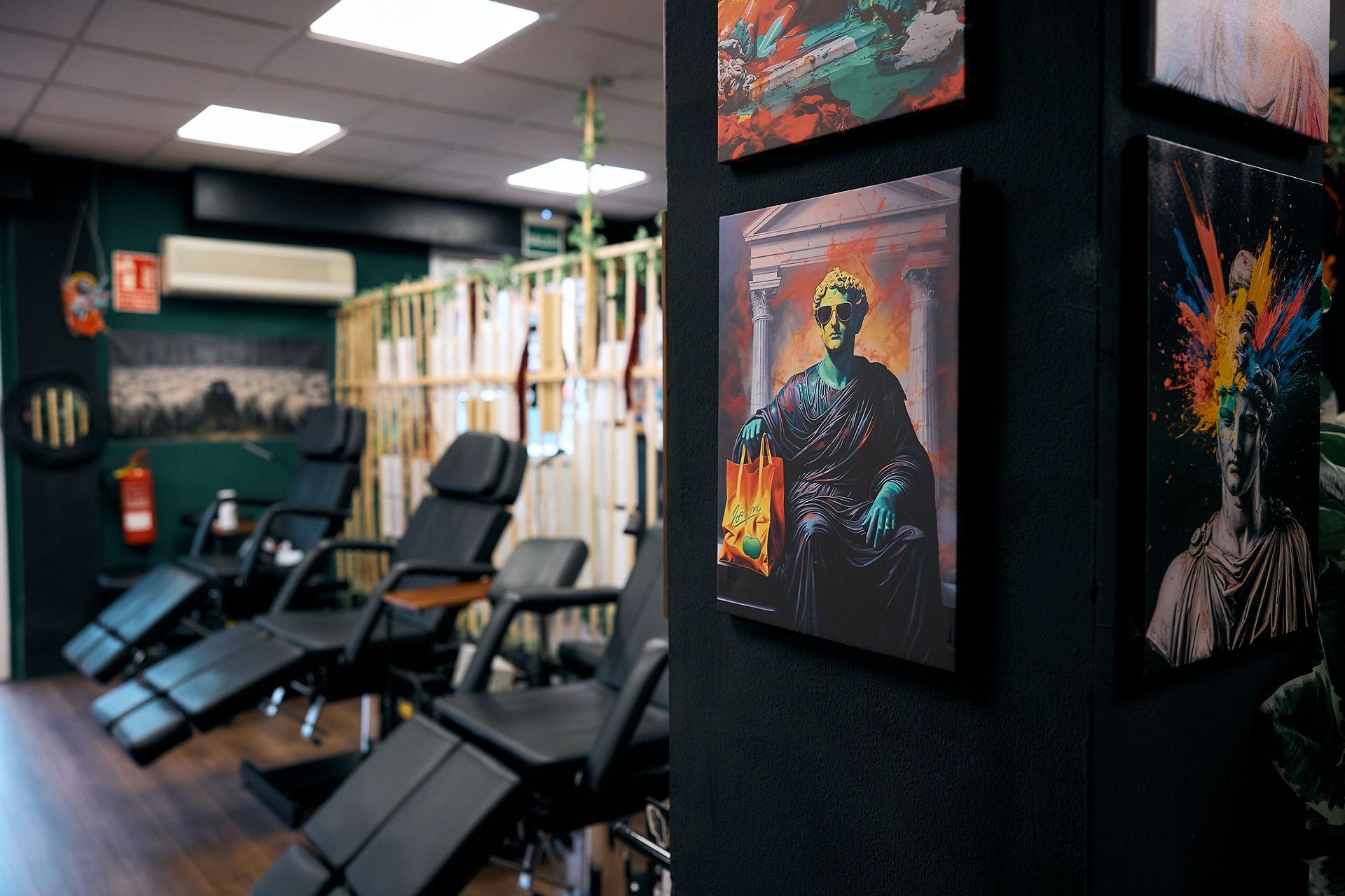 Interior de un estudio de tatuajes con sillas, luces de techo y una colorida obra de arte sobre una columna negra.