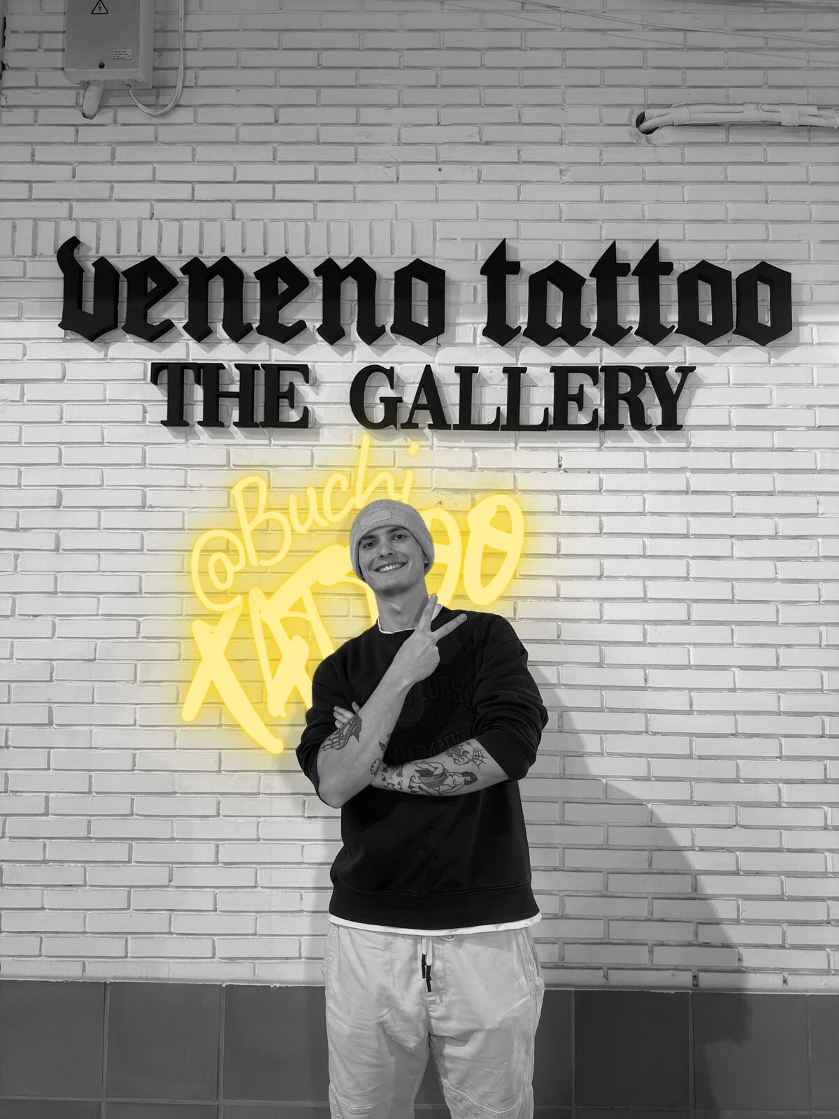 Una persona posando frente a un letrero en una pared de ladrillos que dice 