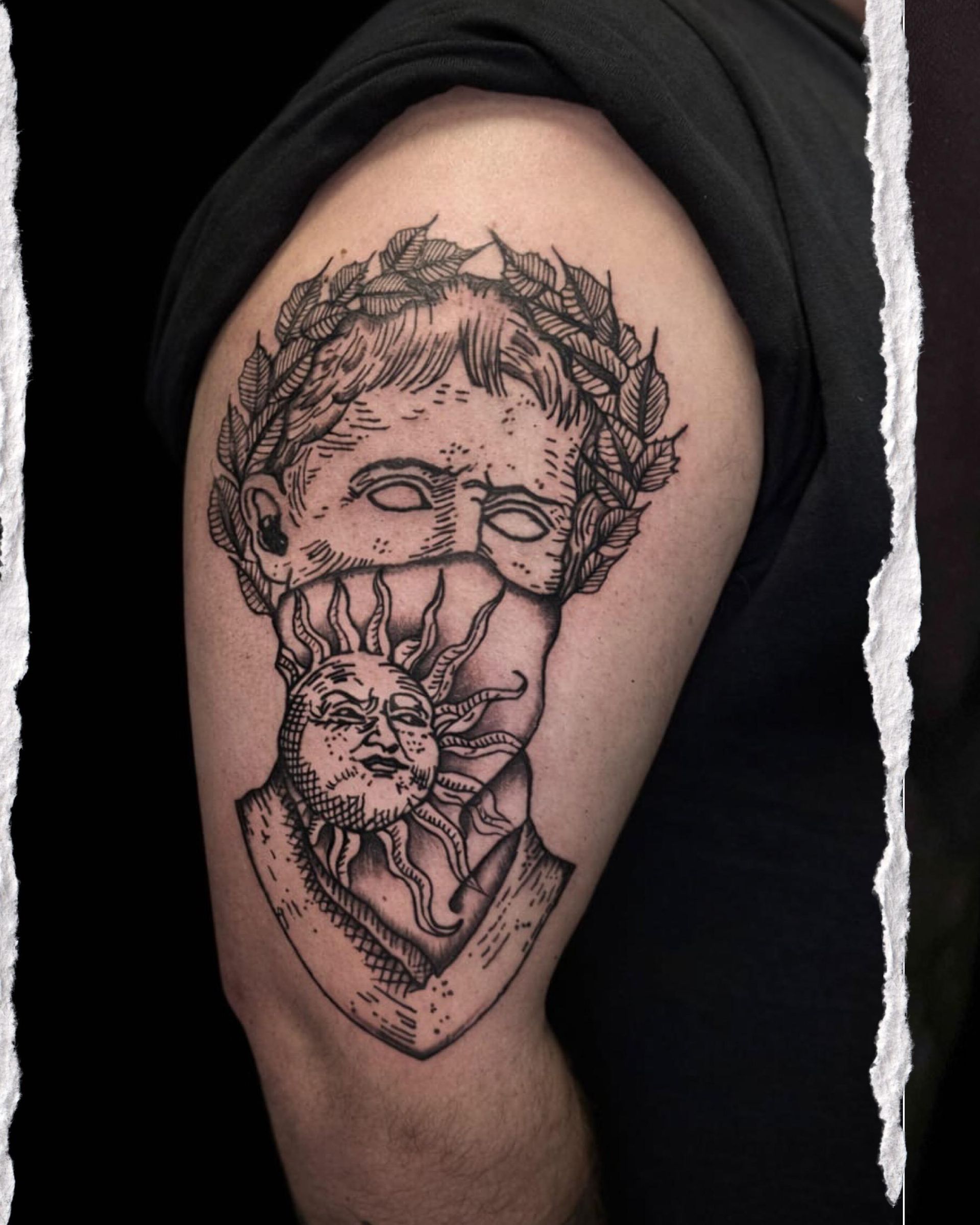 Tatuaje en blanco y negro en la parte superior del brazo que muestra una calavera con una cara más pequeña y un borde en forma de diamante.
