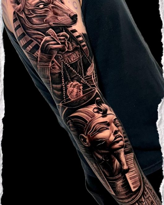 Tatuaje en blanco y negro en el brazo con faraones egipcios y un escarabajo en una manga doblada.