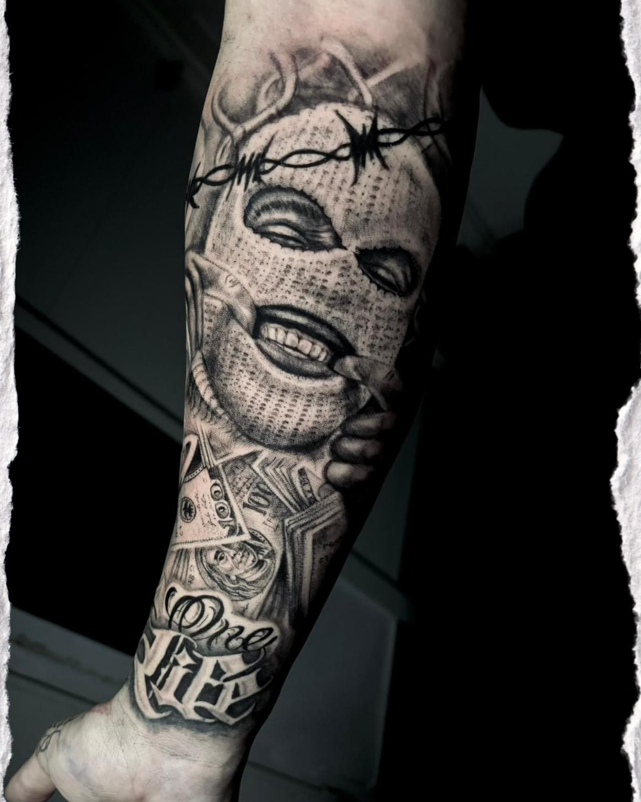 Tatuaje en el brazo con un rostro hecho de alambre de púas y diseños detallados en blanco y negro en el antebrazo.