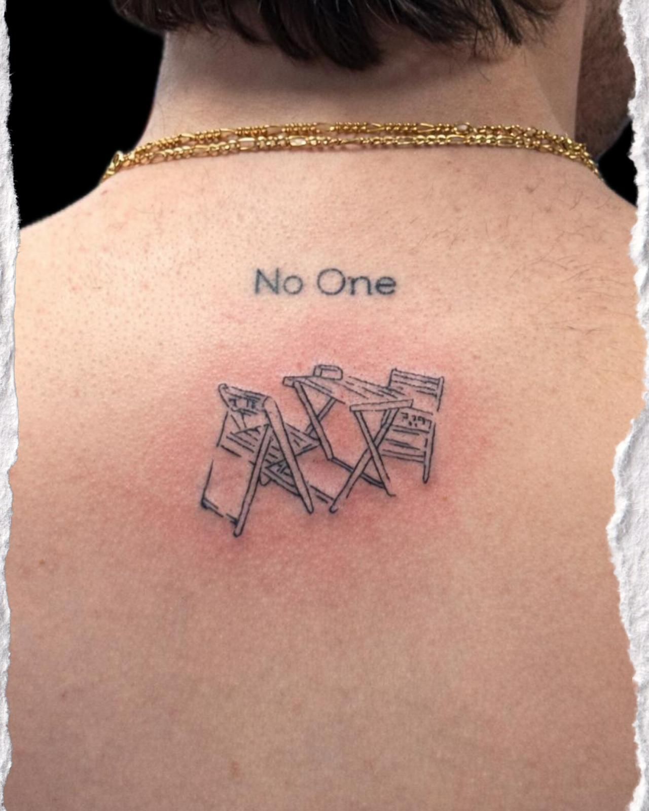 Parte posterior del cuello con cadena de oro, un pequeño tatuaje con el texto "No One" y un rasguño rojo cerca del omóplato.