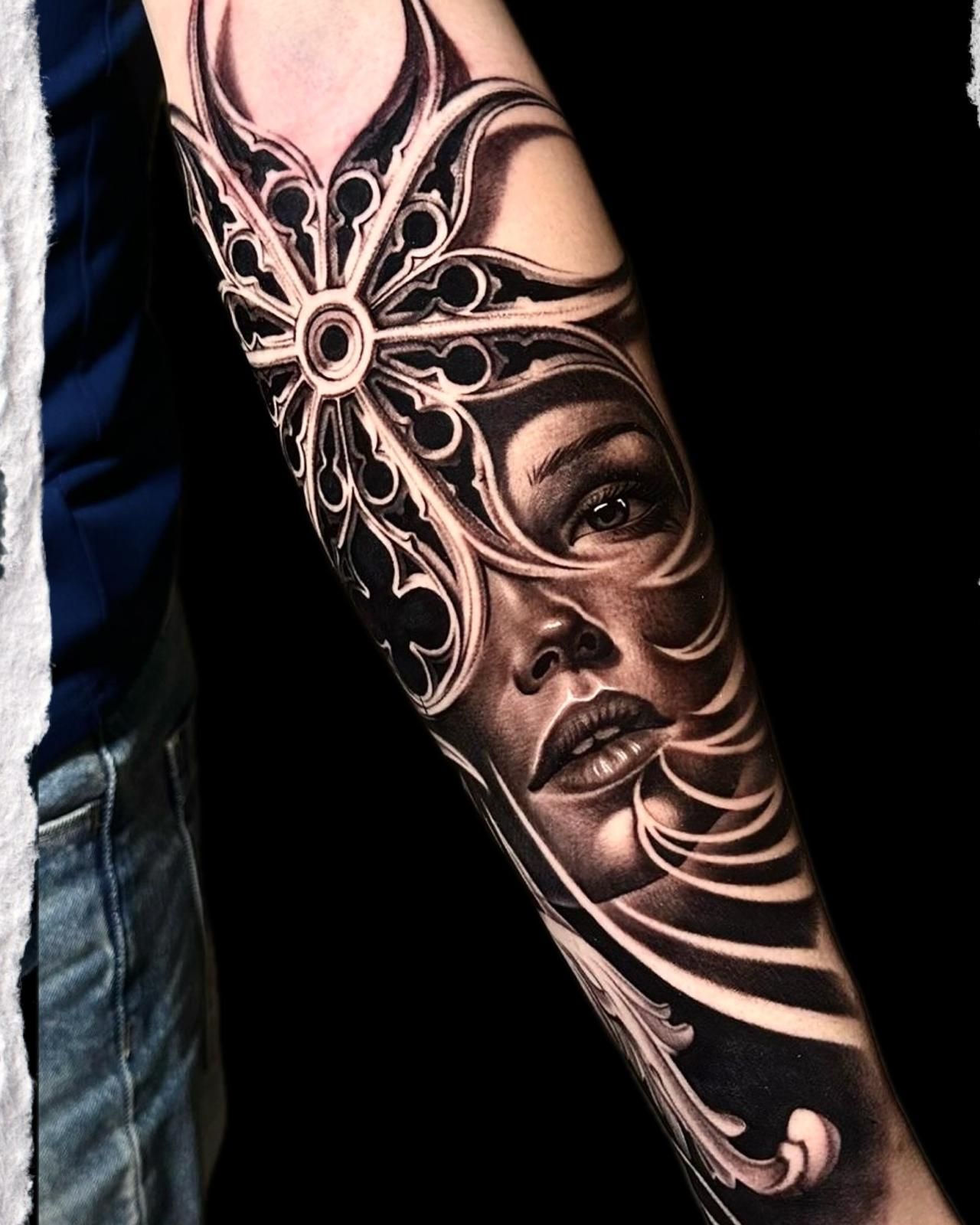 Primer plano de un tatuaje en el antebrazo con un rostro ornamentado en blanco y negro y un diseño floral.