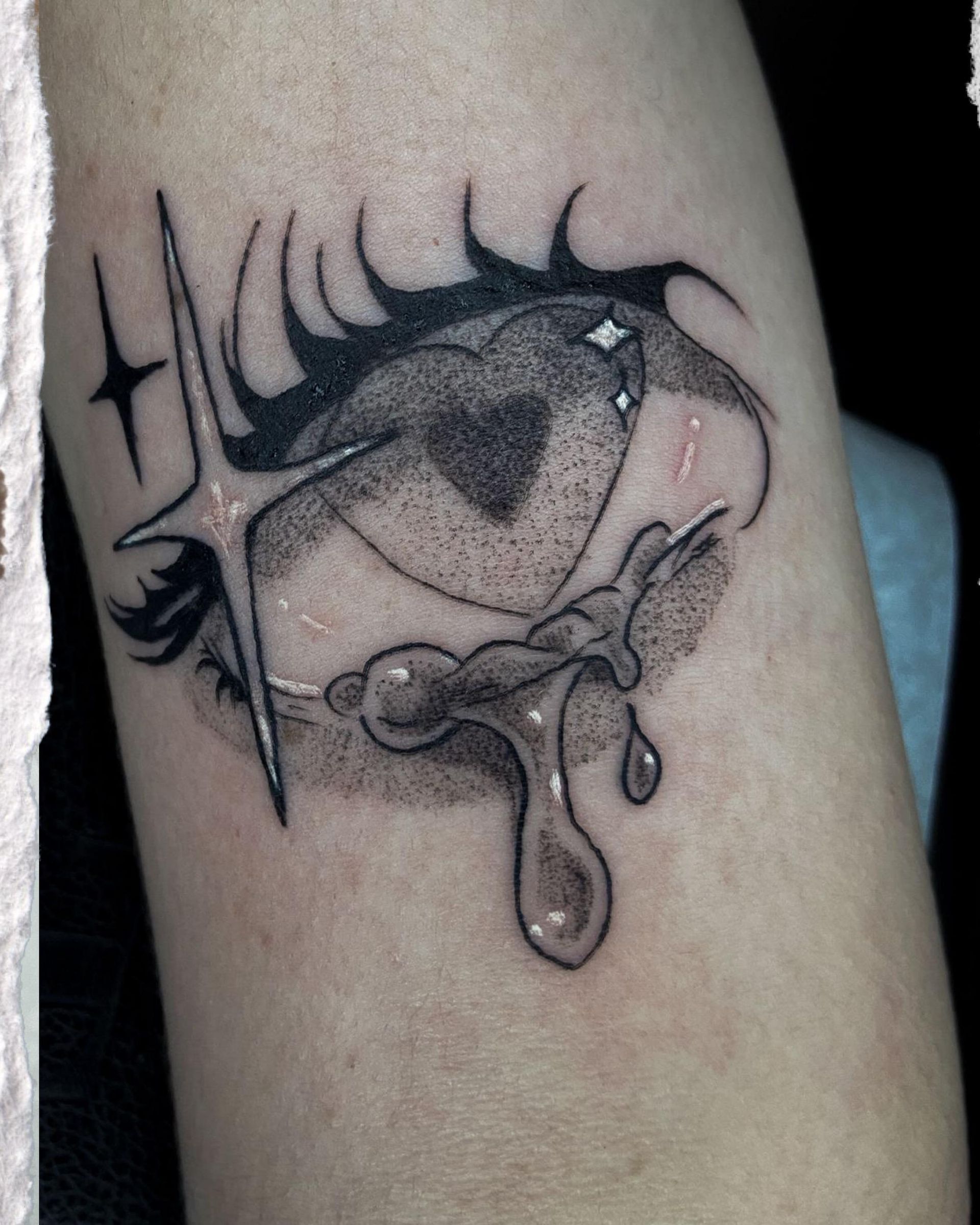 Tatuaje en blanco y negro de un ojo llorando con una estrella y destellos en la piel.