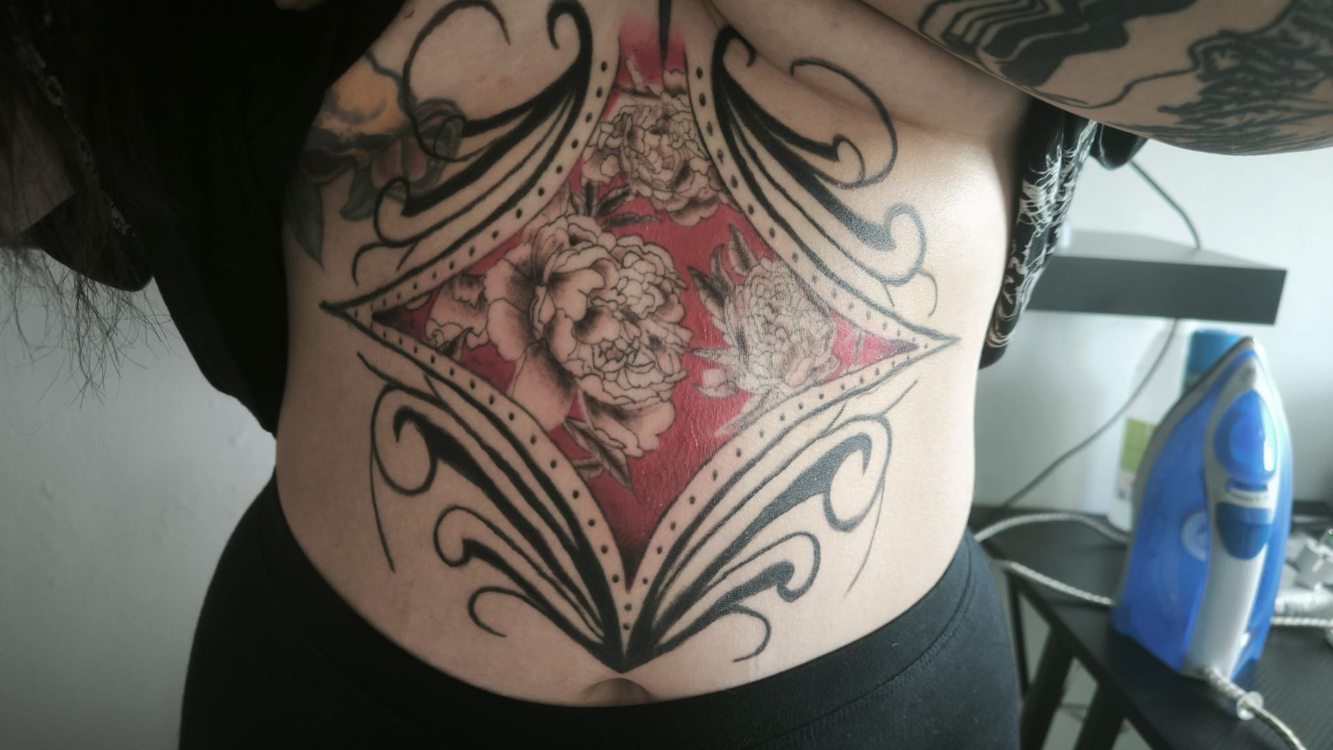 Torso con un gran tatuaje de una rosa enmarcado por espirales ornamentales negras y detalles rojos.