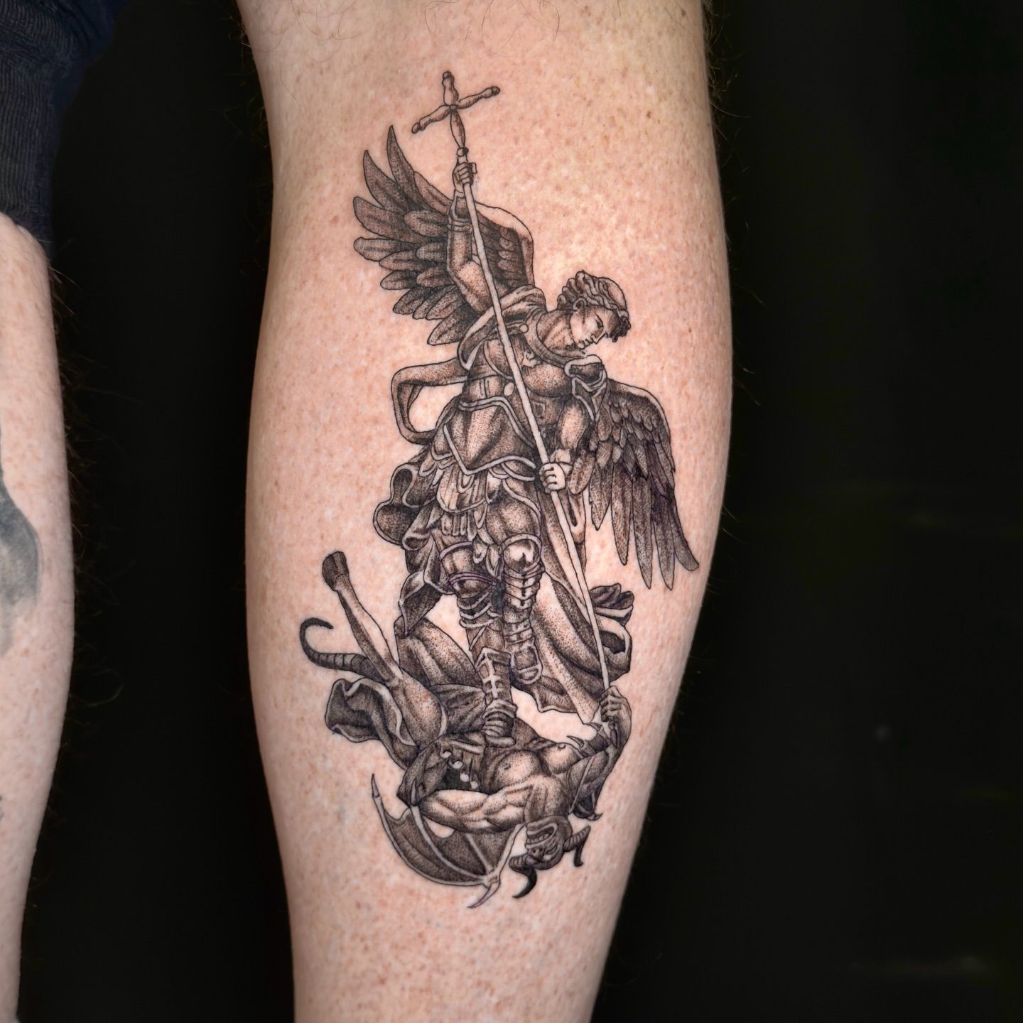 Un tatuaje San Miguel Arcángel derrotando a un demonio alado.
