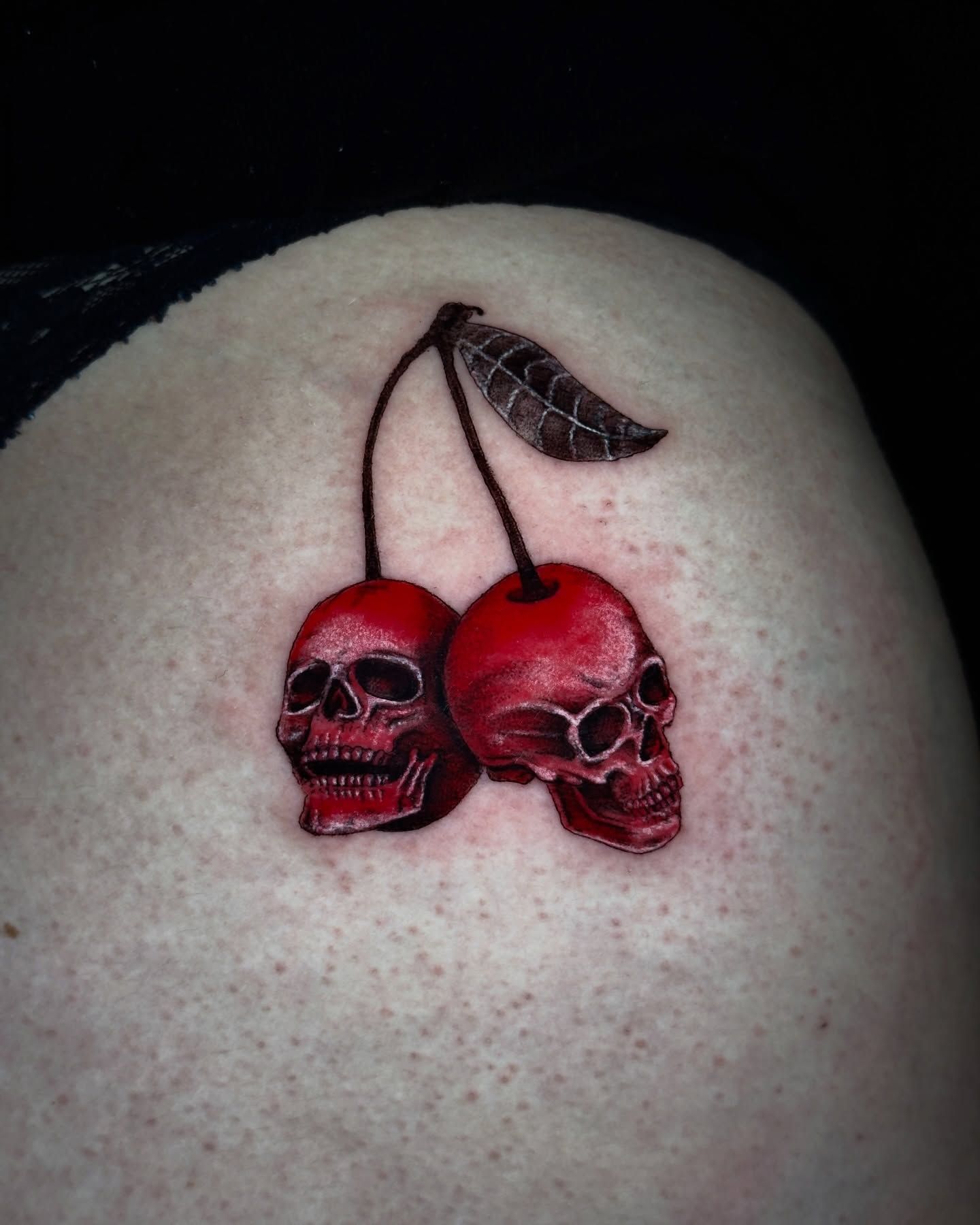 Un tatuaje en la piel de dos calaveras de color rojo intenso con forma de cerezas