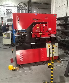 Una máquina roja está en un almacén con un hombre trabajando en el fondo.